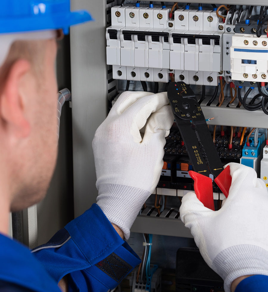 Electrician wearing safety gloves and helmet working on a circuit breaker panel